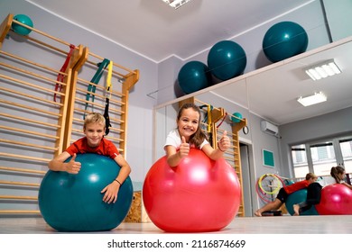 Toddlers boy and girl laying on swiss balls in the gym and showing thumbs up, active kids having good time 