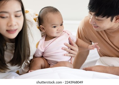 Toddlers are feeling safe and happy with their parents' care in bed at home. Asian family takes care of their children's health with love. Young children are learning to develop their brains. - Shutterstock ID 2243968049