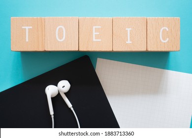 TOEIC listening; Five wooden blocks with TOEIC text of concept, a black notebook, a piece of paper, and a pair of earphones.