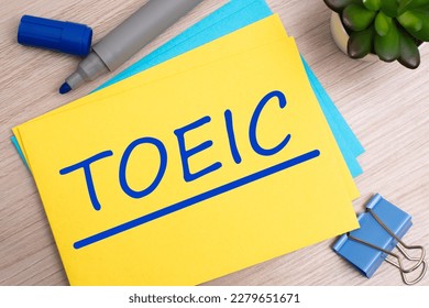 toeic. text on yellow paper on light wooden background with stationery