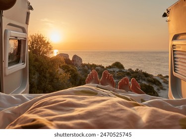 Toes sticking out from under the covers. Couple enjoying a stunning sunrise view from the comfort of their camper van bed, parked by the sea. Relaxing morning with a scenic coastal landscape. - Powered by Shutterstock