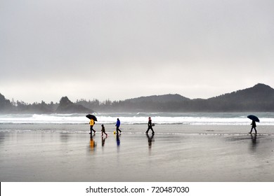 Tofino, Vancouver Island, British Columbia, Canada, 2012. A Happy And Colorful Family Walks Playfully At The Beach In Winter Time Careless Of The Rain And Of The Bad Weather