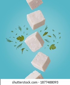 Tofu pieces in motion with chopped parsley and dill falling from above to down on light blue background. Asian, vegan, protein, healthy food, falling and flying in the air.