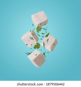 Tofu pieces in motion with dill and parsley on blue background. Asian, vegan, protein, healthy food, falling and flying in the air.
