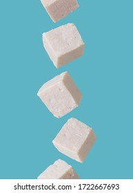 Tofu pieces in motion falling from above to down on blue background. Asian, vegan, protein, healthy food, falling and flying in the air.