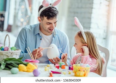 Together and dad we will paint big Easter egg Dad   his little daughter together have fun while preparing for Easter holidays On the table is basket and Easter eggs  flowers   paint 