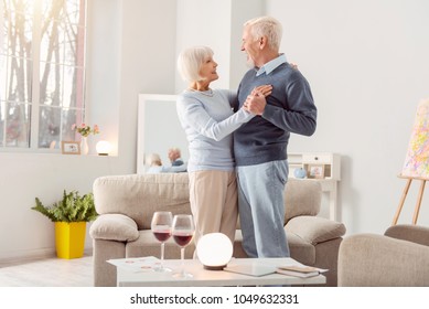 Together forever. Happy elderly couple dancing waltz together in the living room and looking at each other admiringly - Powered by Shutterstock