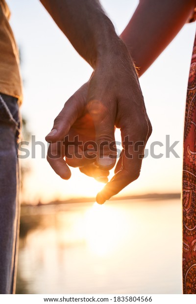 Together and\
forever. Romantic couple holding hands while standing together and\
enjoying the sunset near the\
water