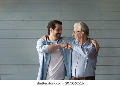 Together we are the power. Bonding mature grandpa young grandson bump fists with smile trust support one another. Happy younger older men relatives friends express unity stand by grey wall. Copy space