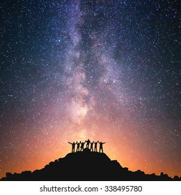 Juntos estamos de pé. Um grupo de pessoas está no topo da colina ao lado da Via Láctea de mãos dadas.