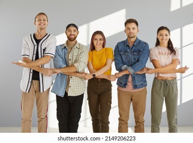 Together We Stand Strong. Team Of Happy, Cheerful Young People Standing In Row And Holding Hands. Studio Group Portrait Of College Friends Standing In Line, Holding Hands And Smiling At Camera