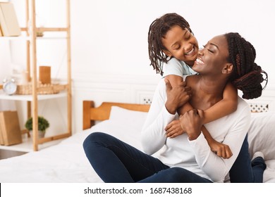 Togetherness Concept. African daughter hugging her mum from the back, sitting on bed, showing her love, empty space