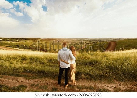 Togetherness Concept. Back view of two lovers standing in field, hugging and looking at landscape, copy space
