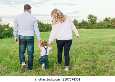 Togetherness With Mom Dad And Toddler Family Walking Away Holding Hands On Grass At Park Or In Yard