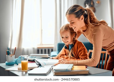 Togetherness while doing home task. Preteen child asking for help from adult female while studying by desktop with glass of juice. Kind mom distracting from housework for helping girl with exercise.