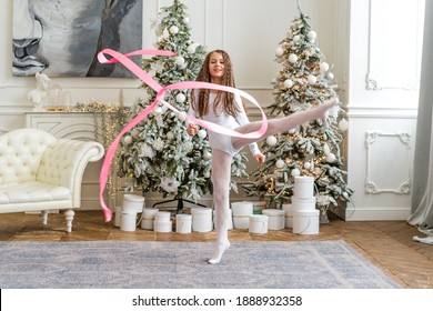 Togliatti, Russia - 31 Dec 2020:A Beautiful Little Gymnast In A White Sports Dress Doing Rhythmic Gymnastics Exercises Spirals With An Artistic Ribbon In A Fitness Class During The Christmas Season. 