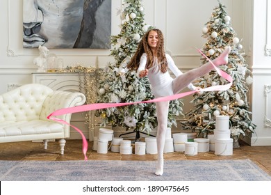 Togliatti, Russia - 31 Dec 2020:A Beautiful Little Gymnast In A White Sports Dress Doing Rhythmic Gymnastics Exercises Spirals With An Artistic Ribbon In A Fitness Class During The Christmas Season. 