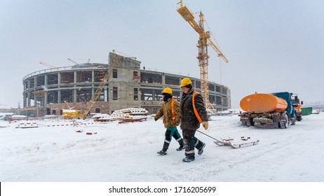 Togliatti, Samara Oblast / Russia - Junuary 17, 2012: Winter panorama of the construction site with cranes and technics. Two workers with wood sled are going along the construction site in a snowfall