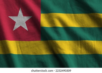 Togo flag with big folds waving close up under the studio light indoors. The official symbols and colors in fabric banner