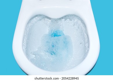 Toilet Bowl Flush With Blue Cleaning Fluid Isolated. Cleaning Toilet Close-up. Environmental Pollution And Water Saving Concept