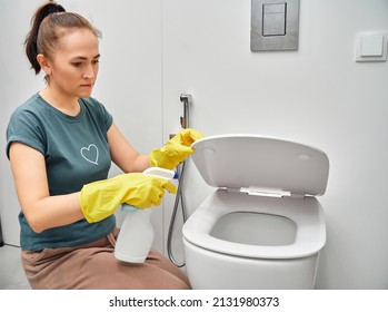 Toilet Cleaning And Disinfection. A Woman Applies A Cleaning Agent With A Sprayer On A Toilet Seat.