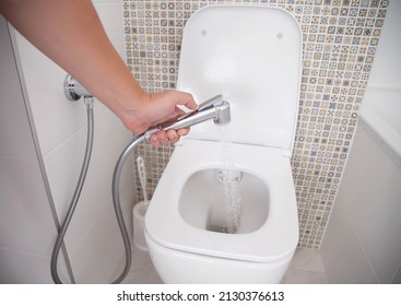 Toilet with a hygienic shower for washing the external genitals. A hand holding a hygienic shower, close-up