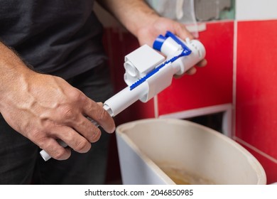 Toilet tank parts replacement. A man in orange gloves repairs the toilet tank drain. - Shutterstock ID 2046850985