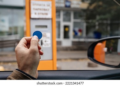 A token for paying for a car parking space in a man's hand from the window. On-site parking toll machine.