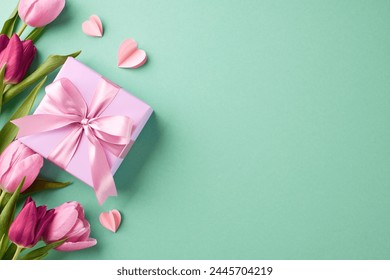 Tokens of gratitude: curated surprises for her. Top view shot of gift box with pink satin ribbon, pink paper hearts, tulips on teal background with space for special occasion greetings messages Foto Stok