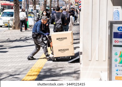 Tokyo, Japan - April 4, 2019: Senior Old Delivery Man Worker Pushing Dolly, Delivering Amazon Boxes Packages In Shinjuku On Street Sidewalk