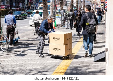 Tokyo, Japan - April 4, 2019: Senior Old Delivery Man Pushing Dolly, Delivering Amazon Boxes Packages In Shinjuku On Street Sidewalk