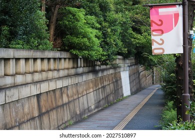 TOKYO, JAPAN - August 19, 2021: Olympic Banner On A Lamppost On A Sidewalk With An Old Stone Wall In Tokyo's Kudanshita Area.