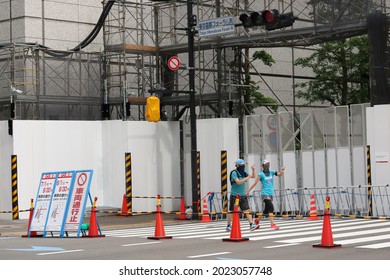 TOKYO, JAPAN - August 7, 2021: People Pass A Closed Street And Tokyo International Forum, The Olympic Weightlifting Venue, Which Is Surrounded By Fences During Tokyo Olympics. Some Motion Blur.