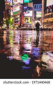 Tokyo, Japan - Circa 2016: Colorful View Of The Famous Shibuya Crossing With A Lonely Person And A Crowd Of People With Umbrellas In The Night With Rain And Reflections In The Floor