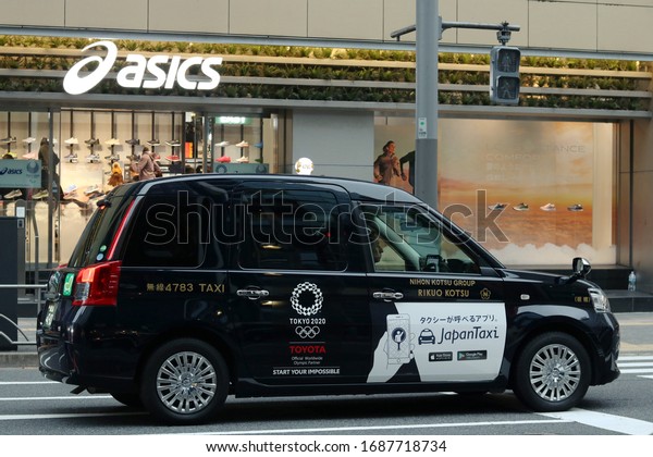 TOKYO,\
JAPAN - December 22, 2019: A taxi in front of an Asics store in\
Tokyo\'s Ginza area. It\'s a Toyota JPN taxi with a 2020 Olympic logo\
on it. A Paralympic logo is in the store\'s\
window.