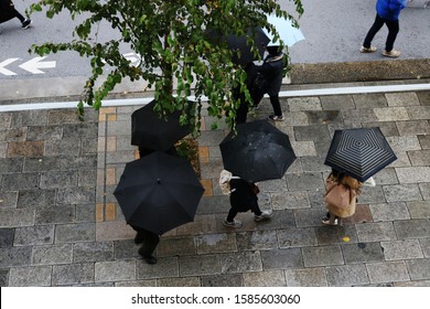 TOKYO, JAPAN - December 7, 2019: Pedestrians Using Umbrellas On A Street In Ginza Seen From Overhead. Some Motion Blur.