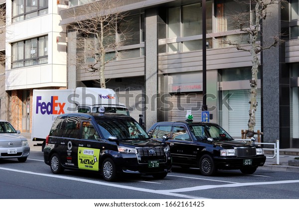 TOKYO, JAPAN -\
February 28, 2020: A pair of taxis and a FedEx delivery truck at a\
junction in Tokyo\'s Kayabacho area. One cab is a Toyota JPN taxi\
with a 2020 Olympic logo on\
it.