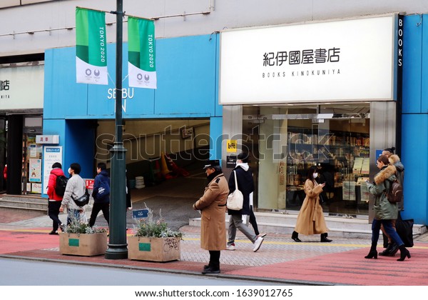 TOKYO, JAPAN - February 7, 2020: A street in\
Tokyo\'s Shibuya area with a Kinokuniya bookstore and an entrance to\
a Seibu department store car park. There are banners promoting the\
Tokyo Olympics 2020.