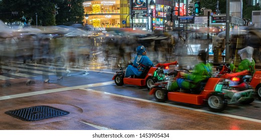 TOKYO, JAPAN - JULY 14TH, 2019. Tourists Driving Rental Go Kart And People Walking Across The Shibuya Scramble Scramble Crossing On A Rainy Night. Long Exposure, Selective Focus.