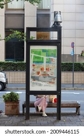 TOKYO, JAPAN - July 16, 2021: Person relaxes on a bench behind a area map on a street in Tokyo's Marunouchi area. There is a security camera above it.