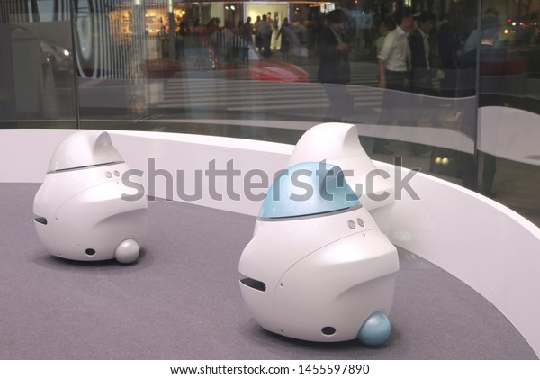 TOKYO, JAPAN - July 19, 2019:\
A group of Nissan EPORO robot cars in Nissan Crossing\'s showroom\
window in Ginza seen in the evening. A busy street can be seen\
outside.