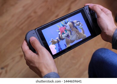 Tokyo, Japan - July 7, 2019 - Man Holding A Black Nintendo Switch Playing Super Smash Brothers With Flooring In The Background