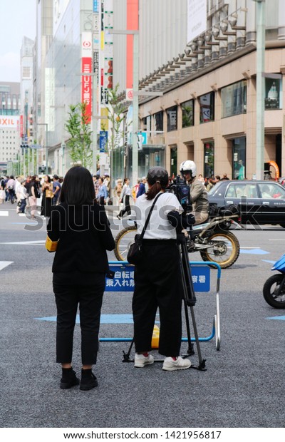 TOKYO,\
JAPAN - June 1, 2019: A TV crew filming a junction in Ginza\
(4-Chome) as traffic passes.. It\'s a so-called pedestrian paradise\
day so some main streets are closed to\
traffic.
