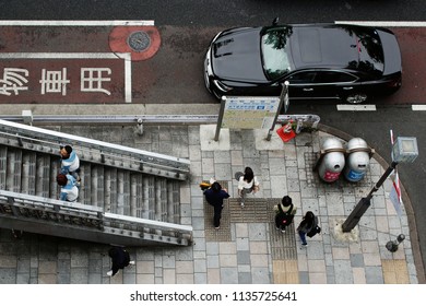 TOKYO, JAPAN - June 16, 2018: Overhead View Of Pedestrian On A Street And Footbridge In Omotesando. A Street Map And Bins Are On The Street Corner.