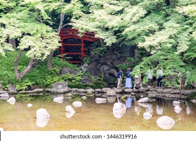 Tokyo, Japan - June 2, 2019: People Cross A Pond Over Stepping Stones In The Koishikawa Korakuen Garden In Bunkyo City Neighborhood