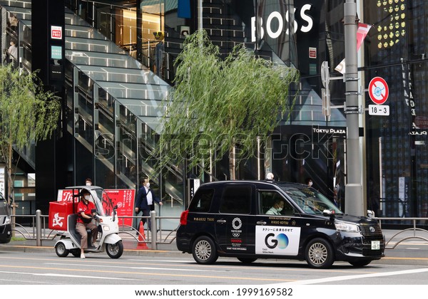 TOKYO, JAPAN - June 29, 2021: Taxi and delivery\
scooter in front of Tokyu Plaza shopping mall where a new Hugo Boss\
store has opened. The car, a Toyota JPN taxi,  has an Olympic 2020\
logo on it.