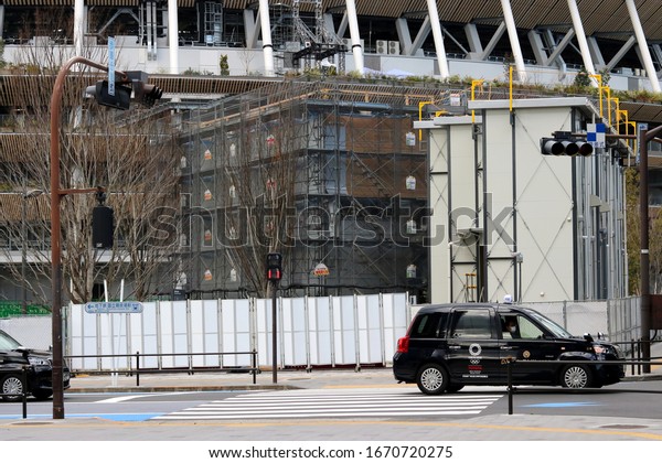 TOKYO,\
JAPAN - March 11, 2020: A Toyota JPN taxi with a 2020 Olympic logo\
going past the site of the new National Stadium which is being\
prepared for the Tokyo Olympics. Some motion\
blur.
