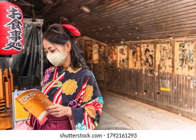 Tokyo, Japan - March 25 2020: Japanese Woman In Hakama Kimono Wearing A Cloth Mask And Reading A Tourist Guide Book Of Tokyo City At Yuraku Concourse Underpass