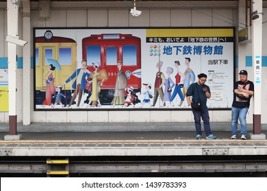 TOKYO, JAPAN - May 18, 2019: People Waiting On Kasai Station's Platform Use Their Smartphones. Behind Them Is A Poster For Tokyo Metro Museum. The Above Ground Station Is Part Of The Subway System.