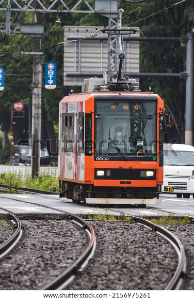 Tokyo, Japan - May, 2022: Orange Tokyo Sakura Tram\
(Toden Arakawa Line) or street car making turn along curved track\
in rainy season